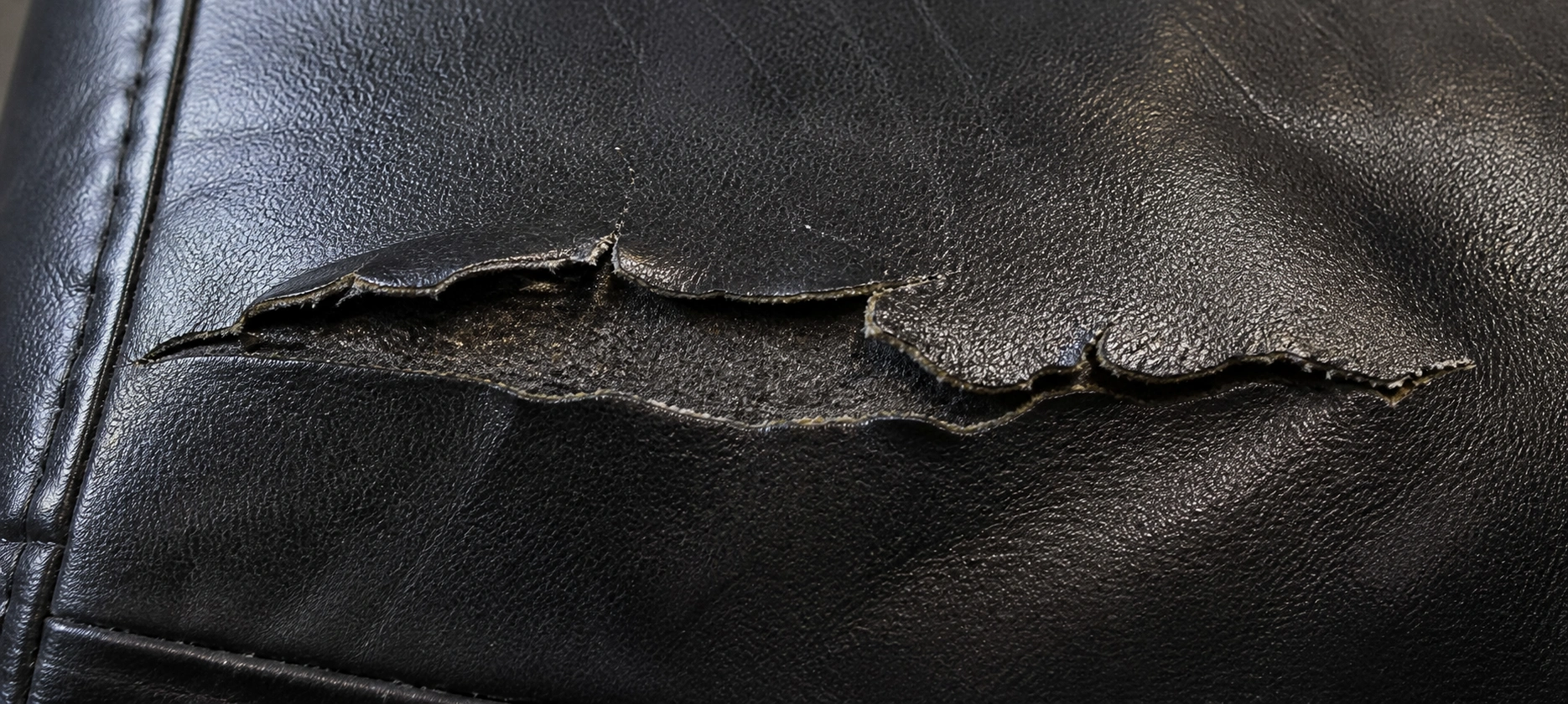 Jagged frayed tear on leather sofa with curled and rough edges from impact damage
