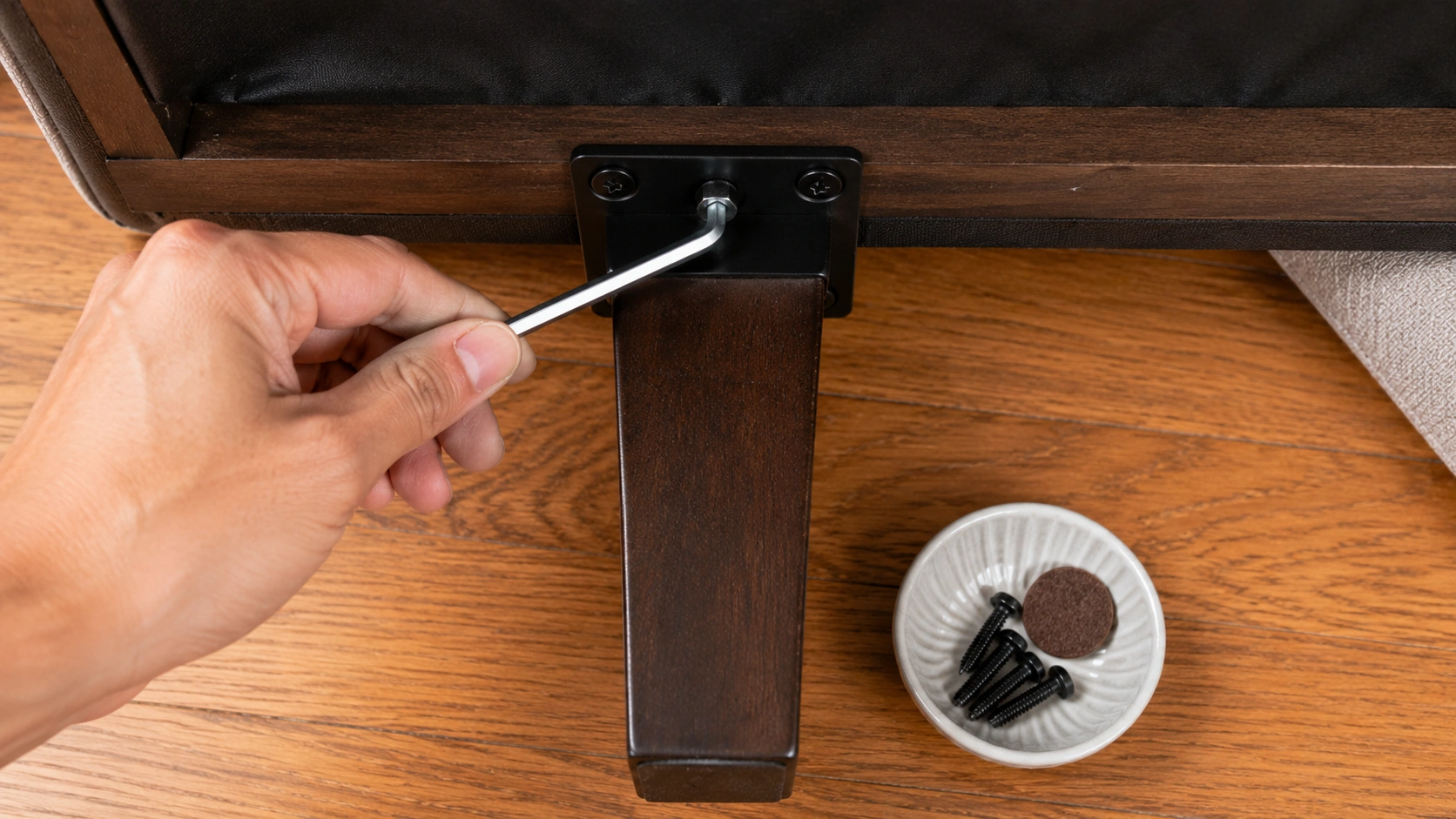 Tightening a loose sofa leg bolt with an Allen wrench to stop squeaking and wobbling