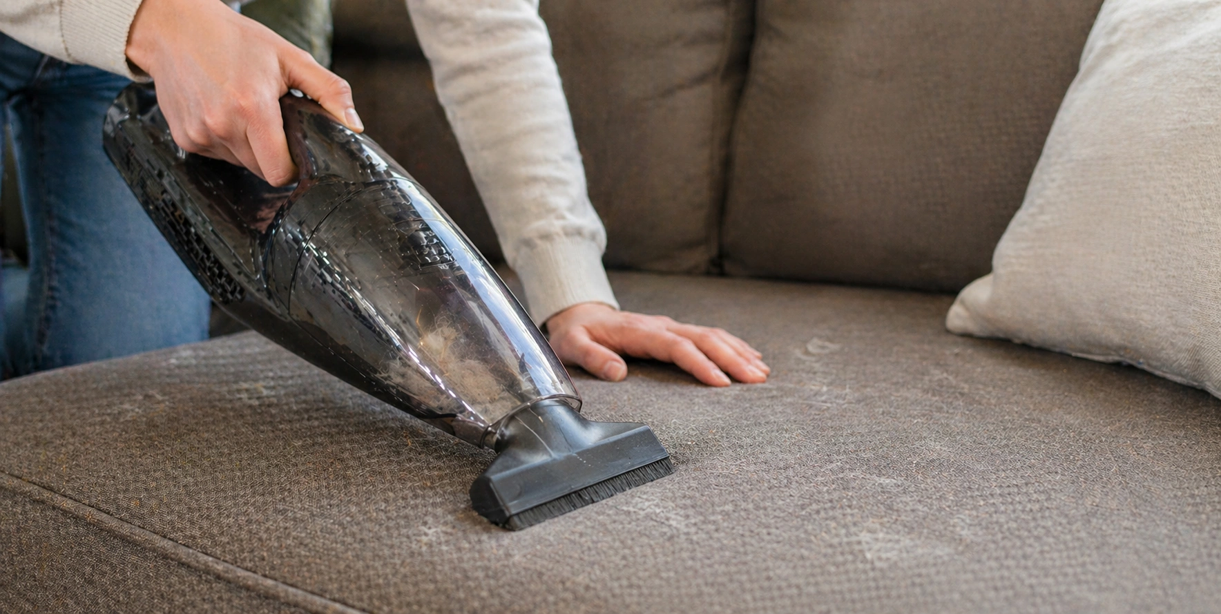 Person vacuuming pet hair from sofa using upholstery attachment tool